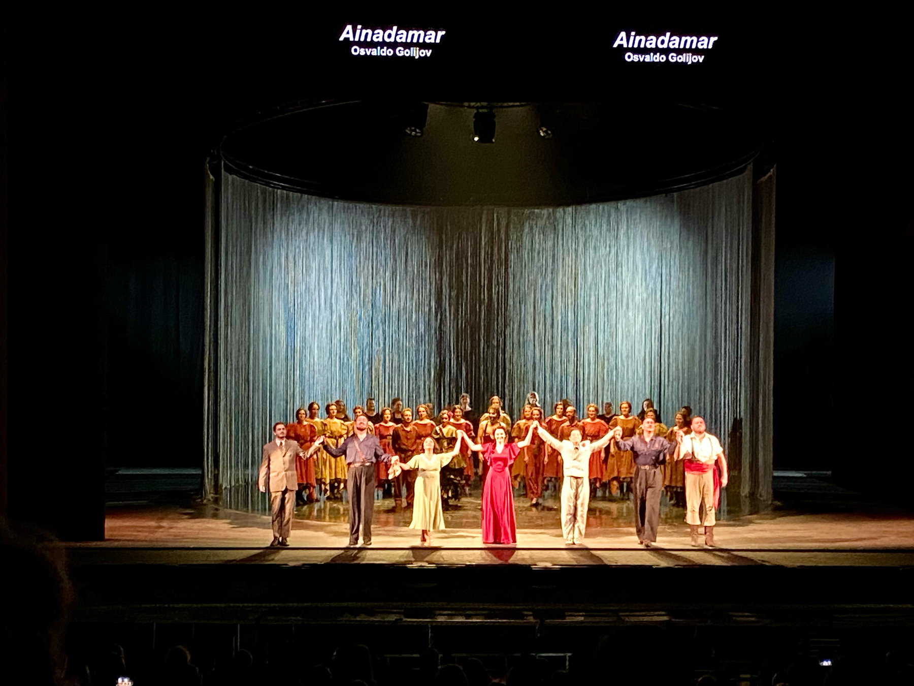 Colourful singers and dancers on brightly lit stage receiving applause at the end of a show
