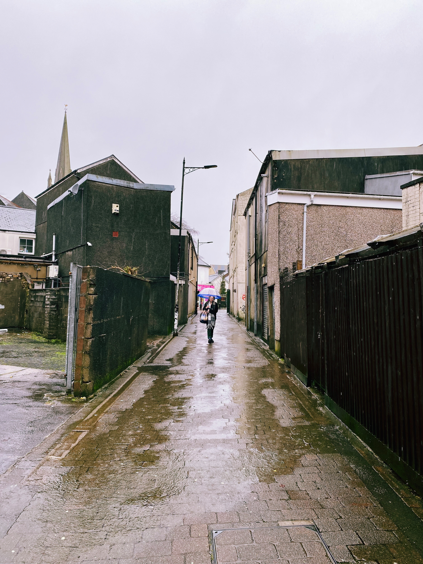 Narrow alleyway in the rain. Puddles. Woman walking with umbrella.