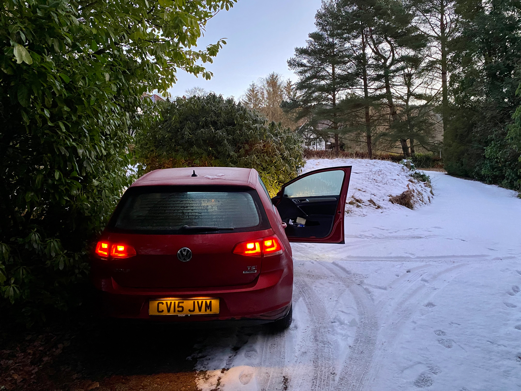 Red car at bottom of snow covered sloping driveway