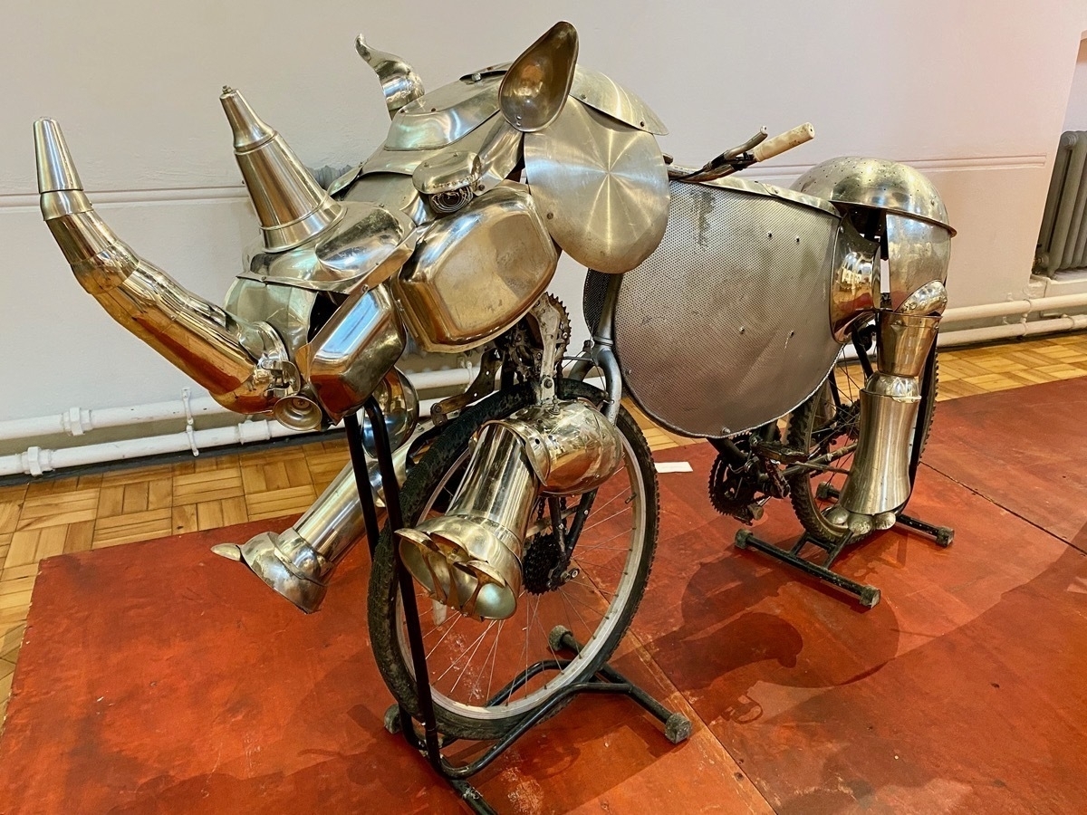 Metal sculpture of a rhino constructed using reflective stainless steel objects attached to a bicycle