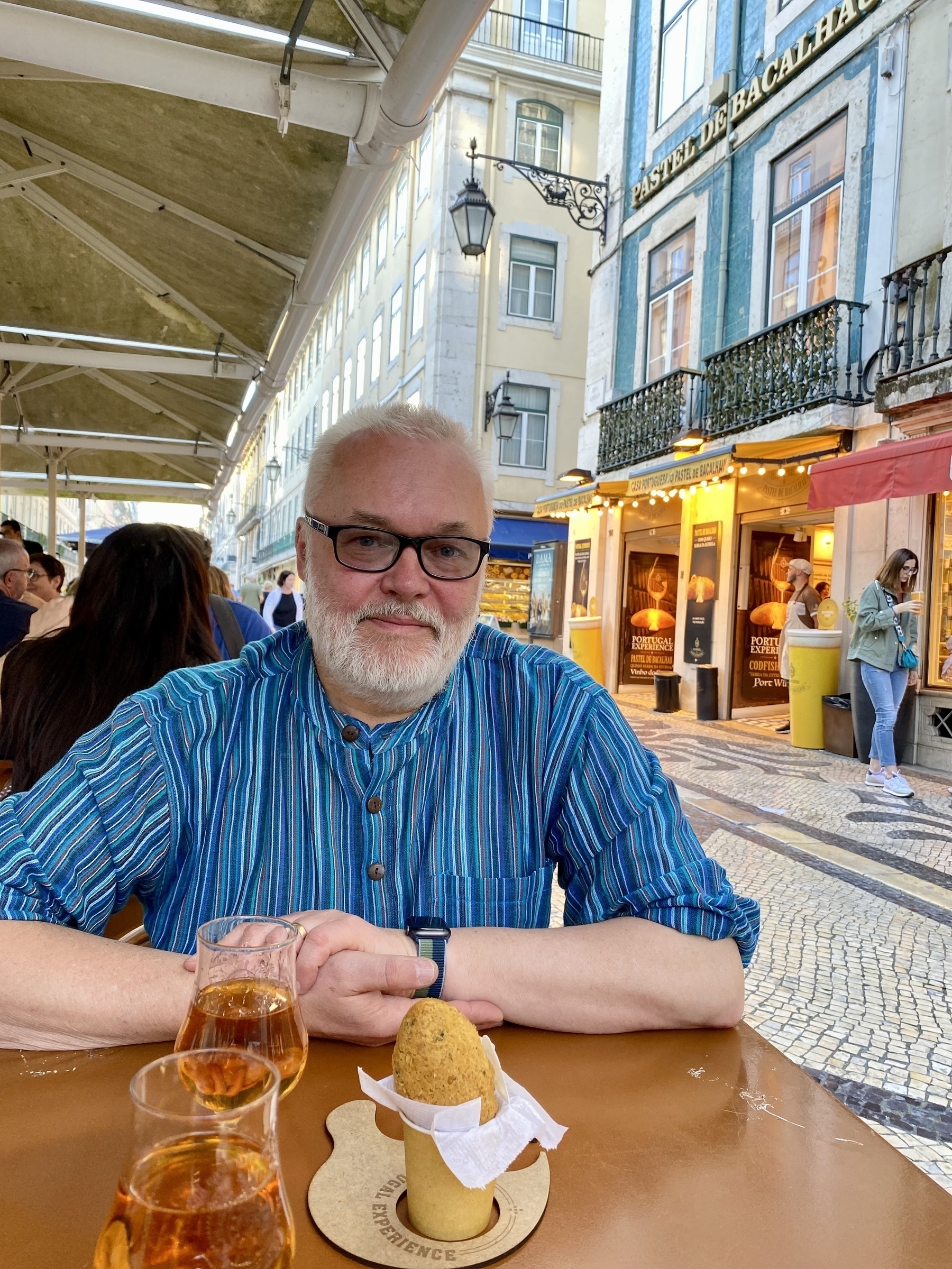 Man seated at table in street with glasses of white port and cod fishcake