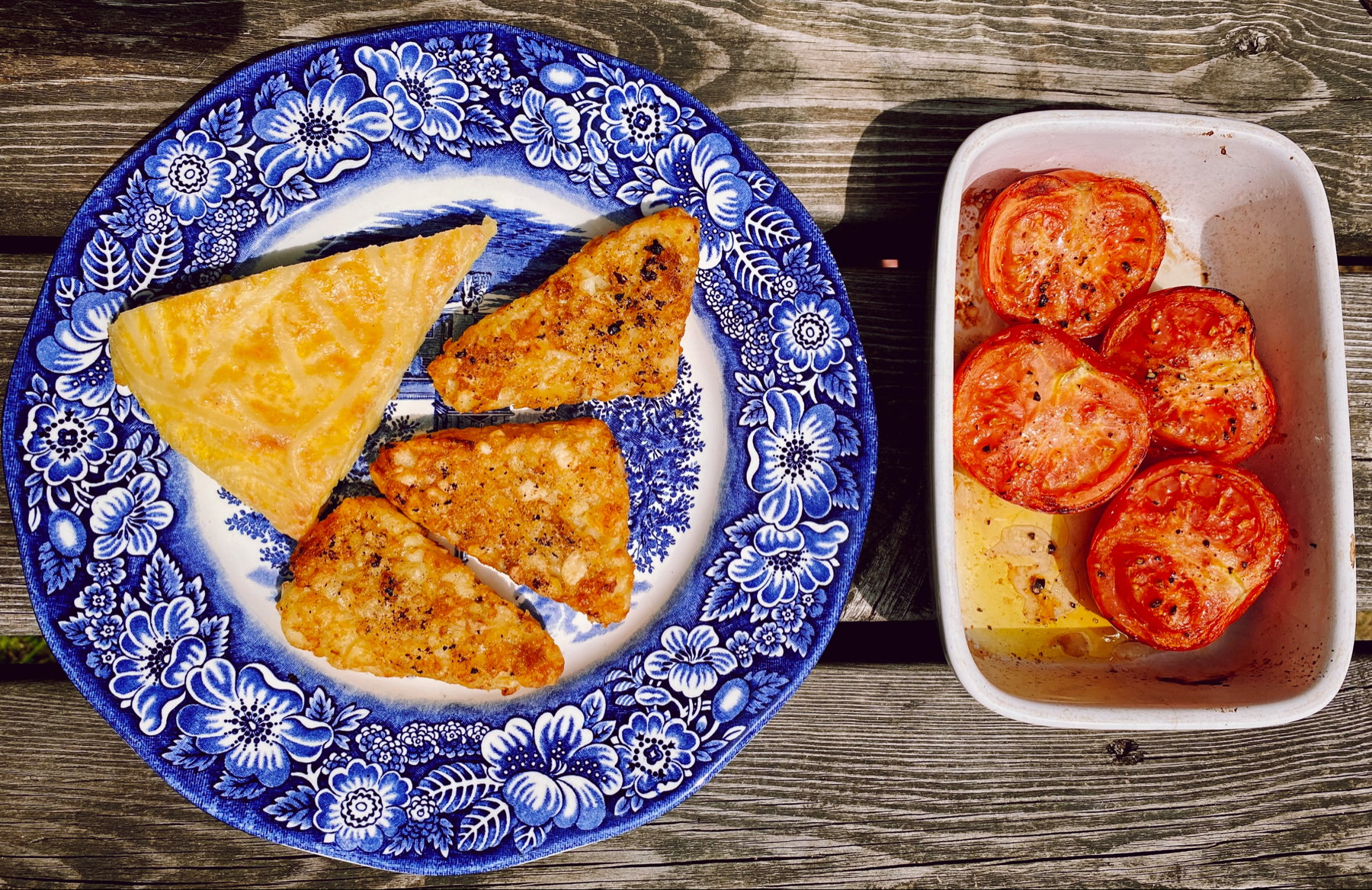 Willow pattern plate of hash browns and omelette slice next to dish of roasted tomatoes