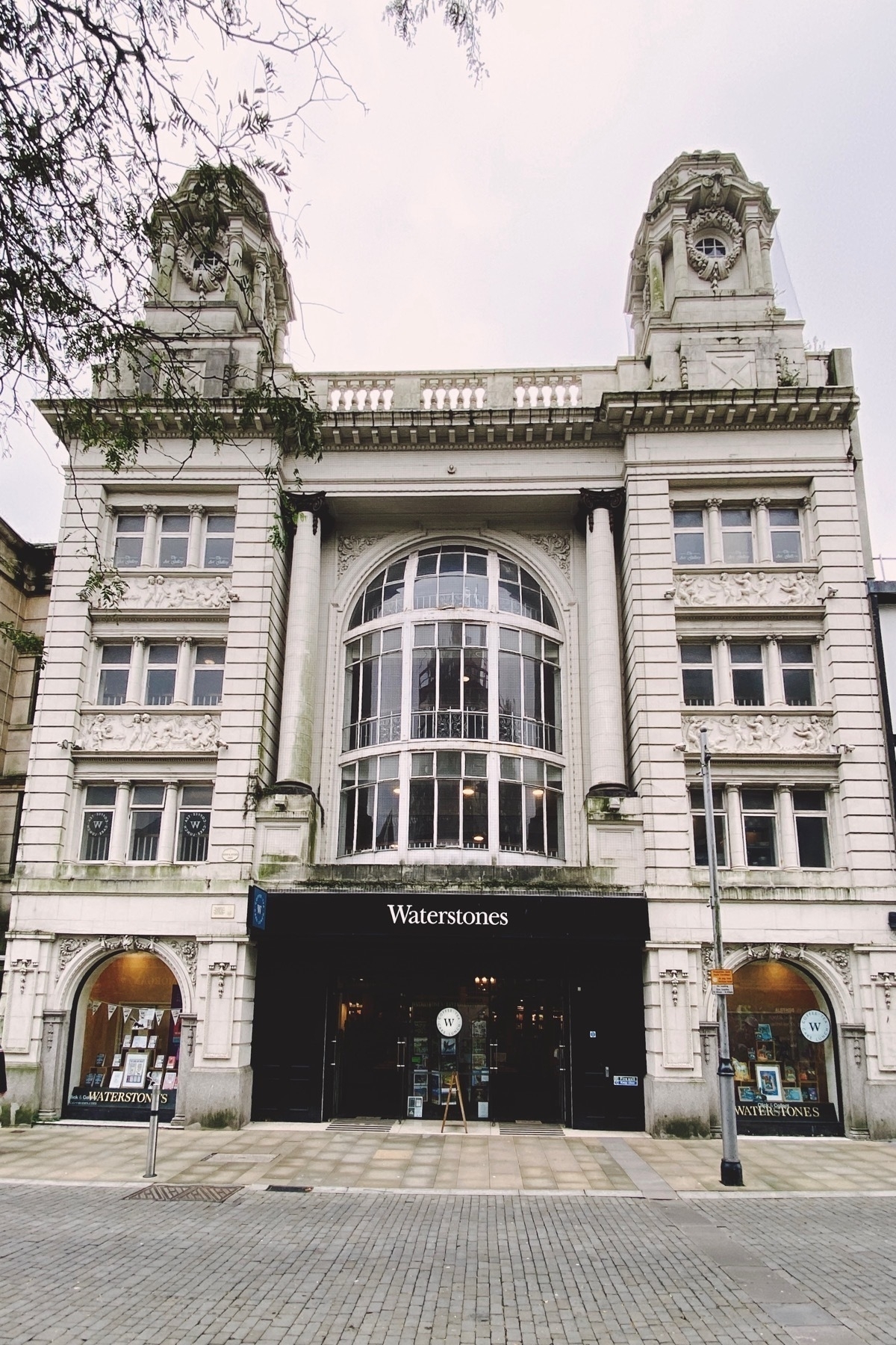 White stone, ornate historical building with central large curved glass window on upper floors.Modern bookshop entrance at ground level.